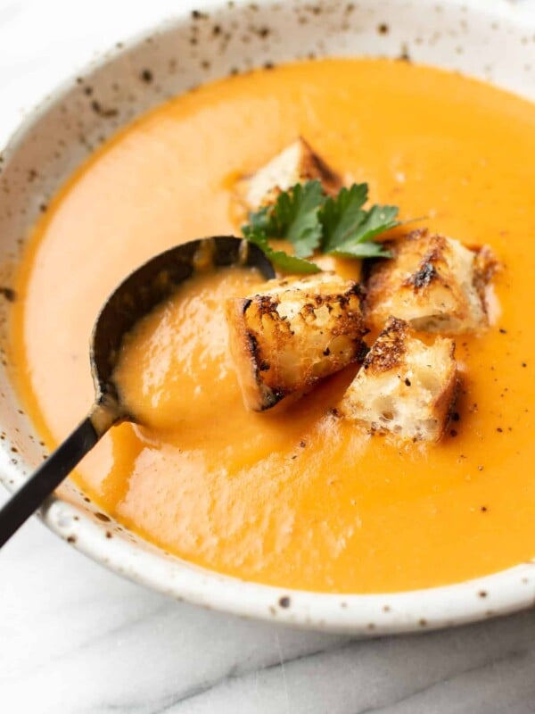 a bowl of potato leek tomato soup with croutons and a spoon