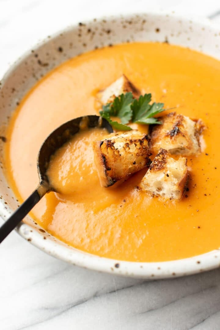 a bowl of potato leek tomato soup with croutons and a spoon