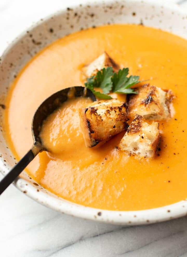 a bowl of potato leek tomato soup with croutons and a spoon
