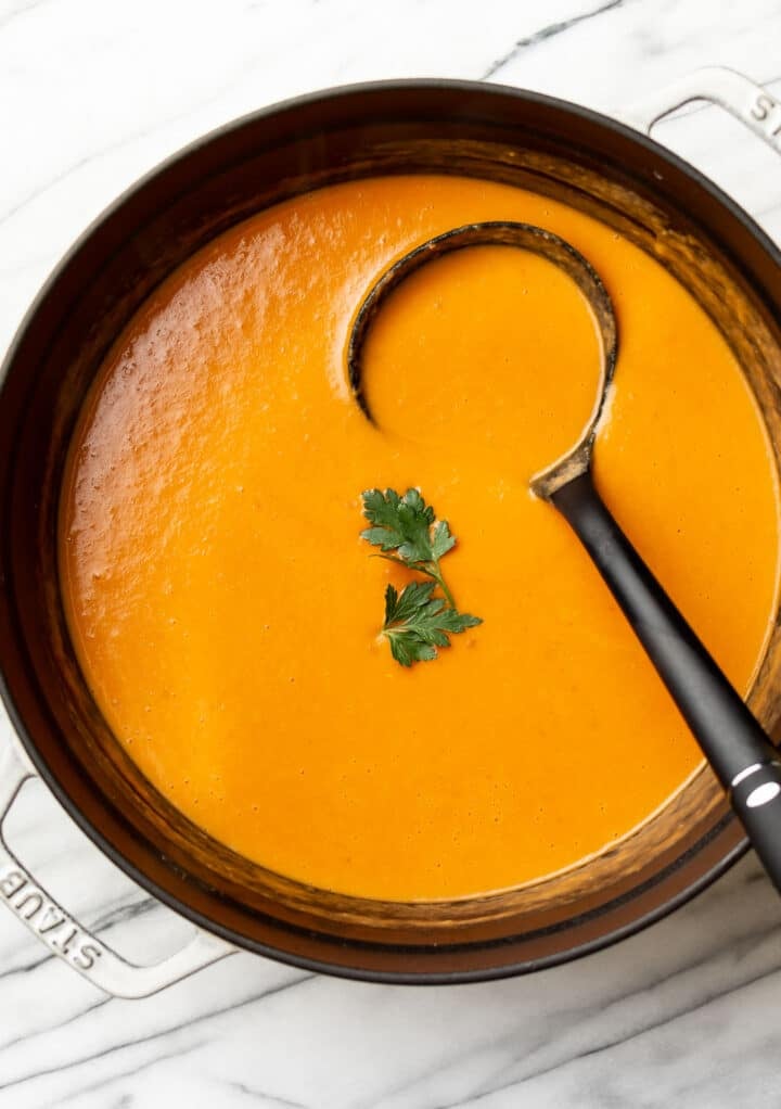 a pot of tomato, leek, potato soup with a ladle