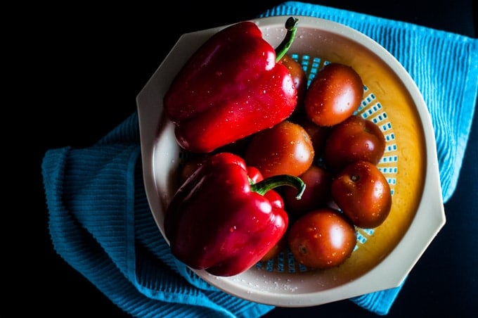 a colander with two red peppers and whole tomatoes