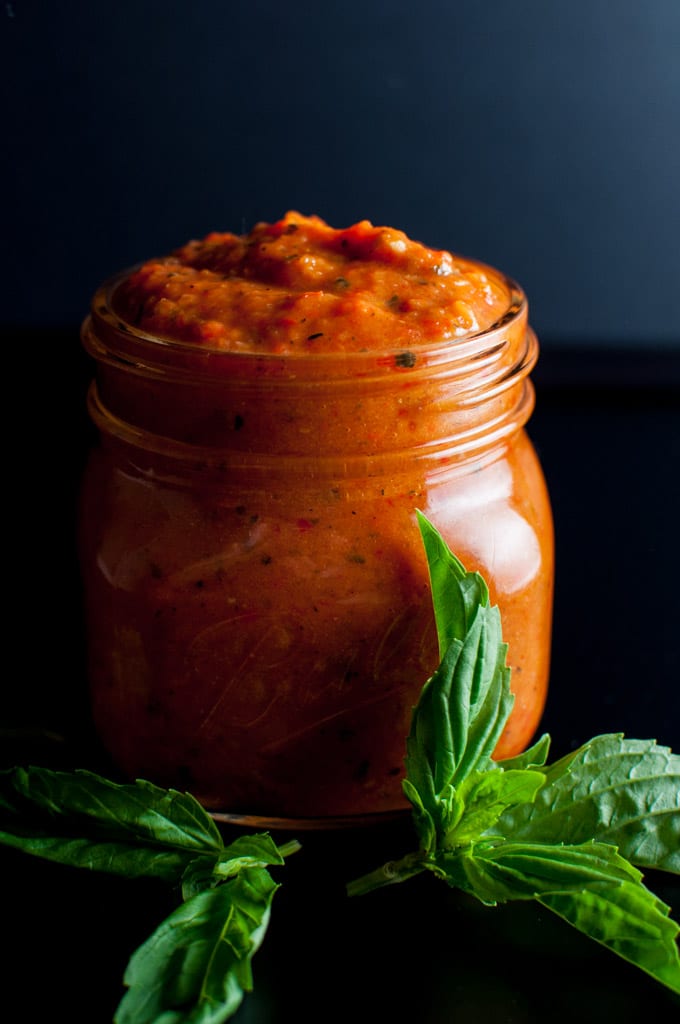 close-up of a glass jar of homemade roasted red pepper and tomato sauce with basil leaves