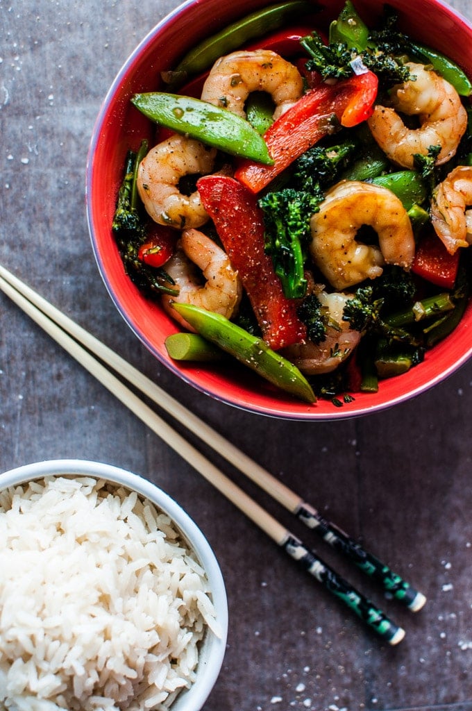 Chinese style skinny shrimp and vegetable stir fry in a red bowl with rice and chopsticks