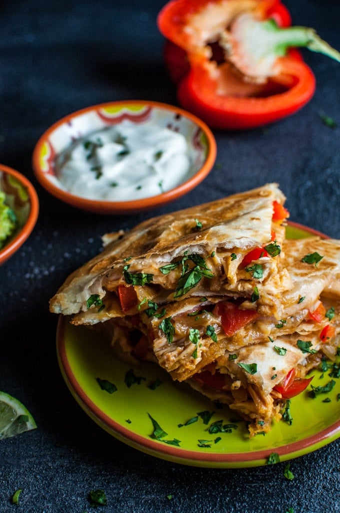 close-up of cheesy chicken fajita quesadilla on a plate with bowls of guacamole and sour cream