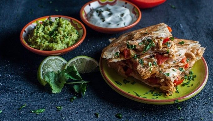 plate with chicken fajita quesadilla and bowls of guacamole and sour cream with lime wedges