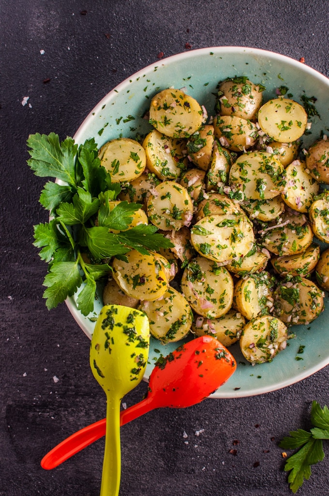 chimichurri potato salad in a bowl with two serving spoons and parsley garnish