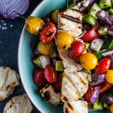 Greek salad with grilled halloumi and tomato skewers in a blue bowl