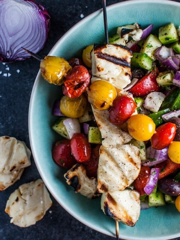Greek salad with grilled halloumi and tomato skewers in a blue bowl