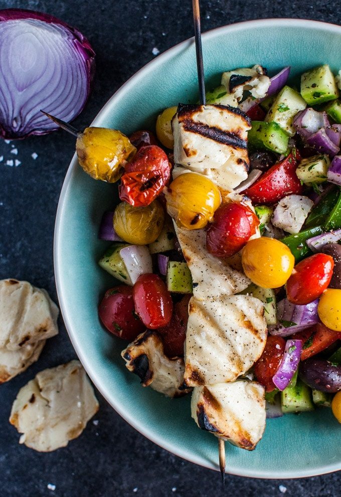 Greek salad with grilled halloumi and tomato skewers in a blue bowl