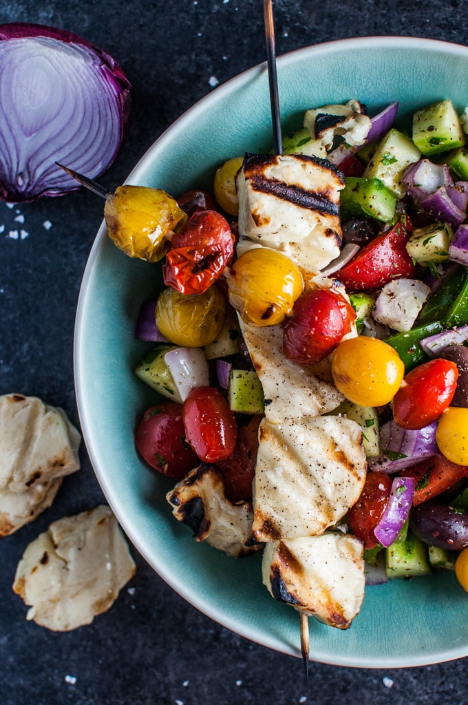 close-up of grilled halloumi and tomato skewers on a bowl of Greek salad