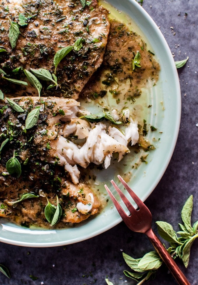 close-up of tilapia with lemon herb butter sauce and a fork