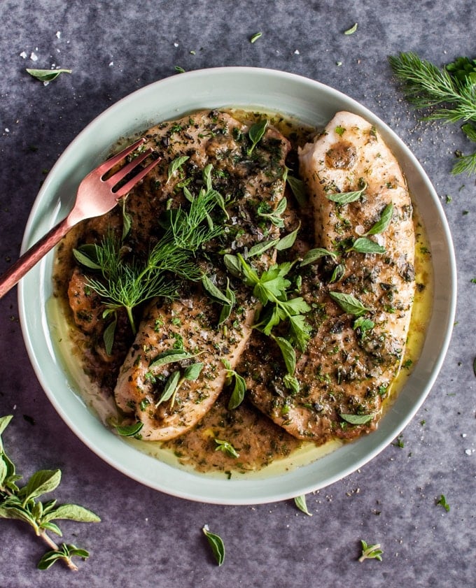 tilapia fish with a lemon butter herb sauce on a plate with a fork