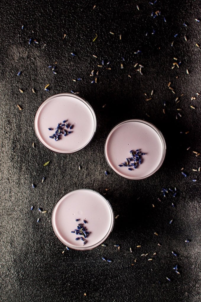 three glass containers of lavender panna cotta on a dark surface