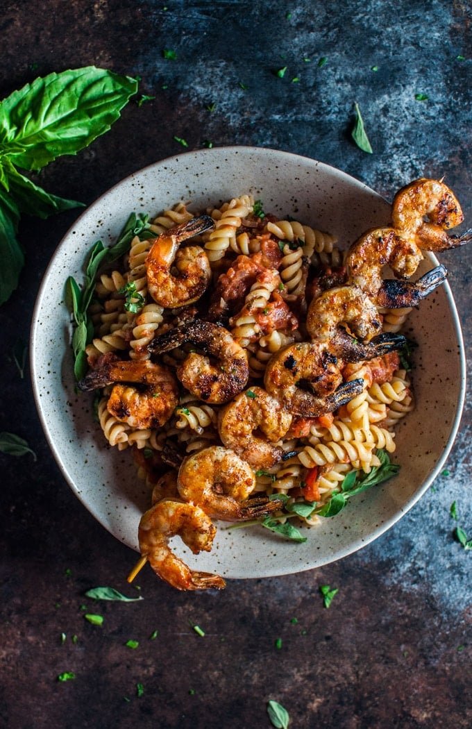 beige bowl of spicy pasta with grilled shrimp on a skewer