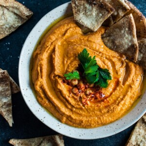 bowl of roasted red pepper and sriracha hummus with pieces of pita bread