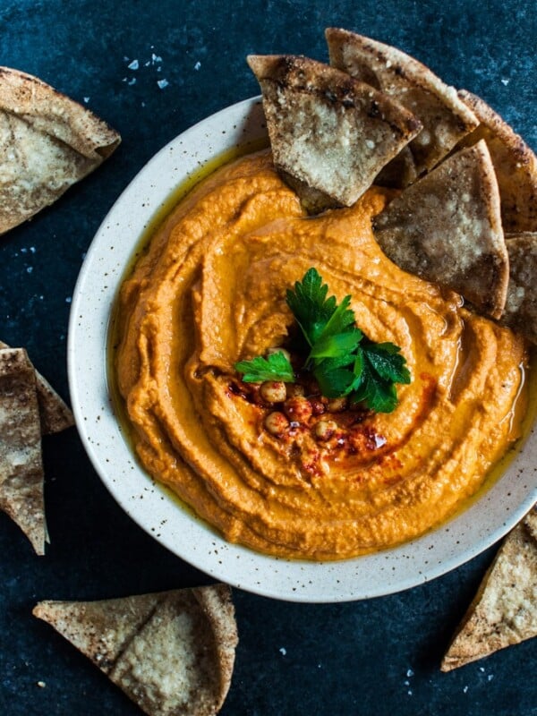 bowl of roasted red pepper and sriracha hummus with pieces of pita bread