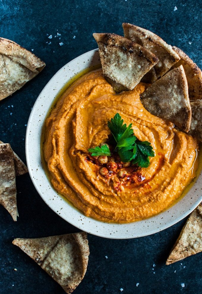 bowl of roasted red pepper and sriracha hummus with pieces of pita bread