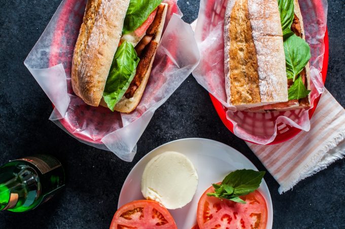 two Caprese sandwiches with bacon, mozzarella, basil, and tomatoes