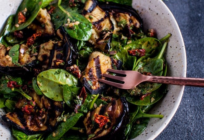 close-up of grilled eggplant and spinach salad with a paprika lemon dressing and a fork