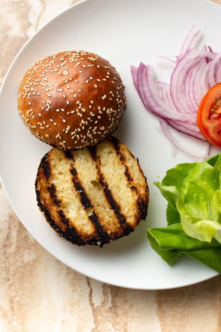 homemade ground chicken burger toppings on a plate (bun, lettuce, tomato, red onions)