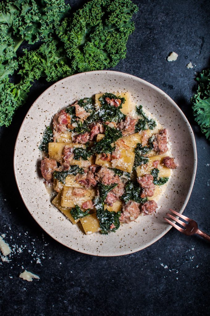 bowl with rigatoni and sausage, bacon, and kale with a fork