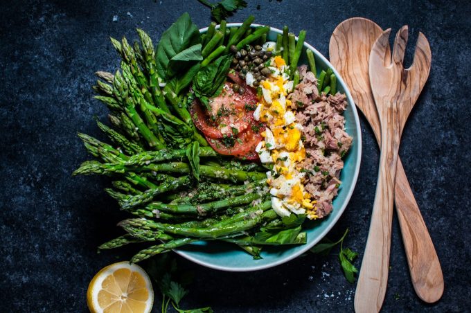 teal bowl of healthy asparagus and green bean salad next to half a lemon and wooden salad utensils