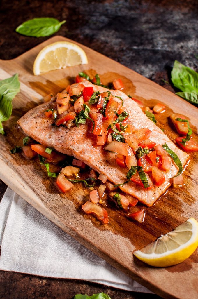 a piece of bruschetta salmon on a wooden board with lemon wedges