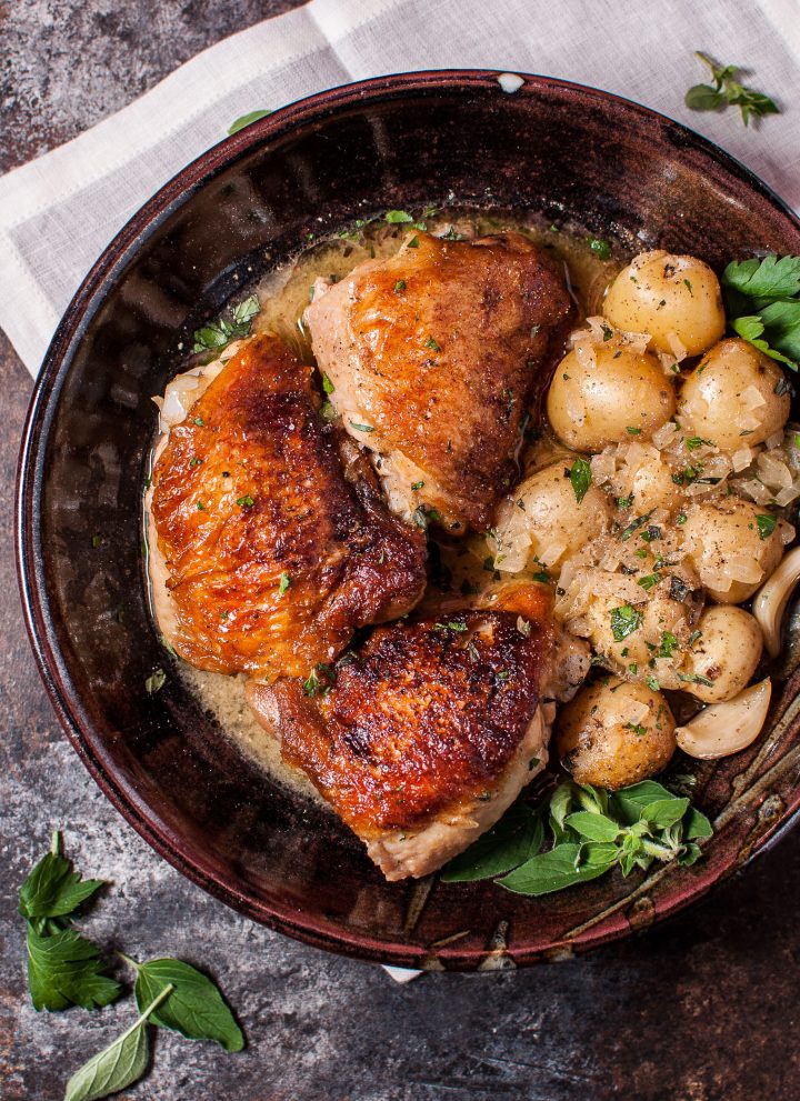 crispy lemon herb chicken with little potatoes in a brown bowl