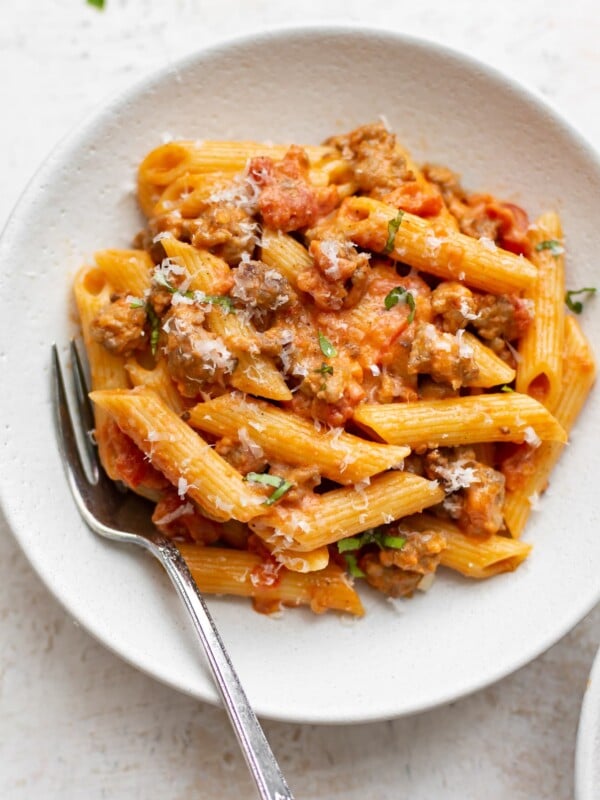 spicy Italian sausage penne pasta with a fork in a white bowl