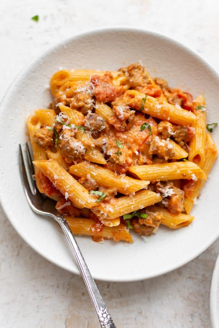 spicy Italian sausage penne pasta with a fork in a white bowl