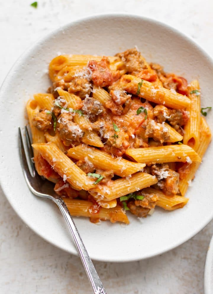 spicy Italian sausage penne pasta with a fork in a white bowl