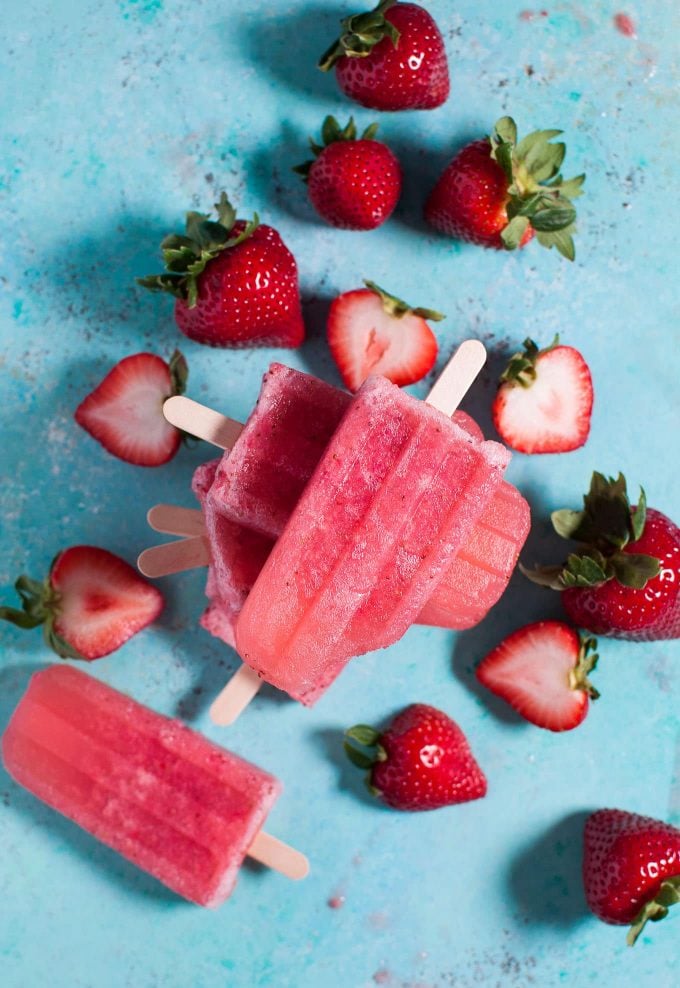 stack of several strawberry moscato popsicles next to many strawberries