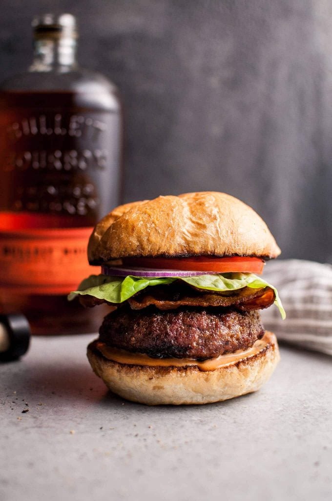 BBQ bourbon burger with lettuce, tomato, and onion with a bottle of bourbon in the background