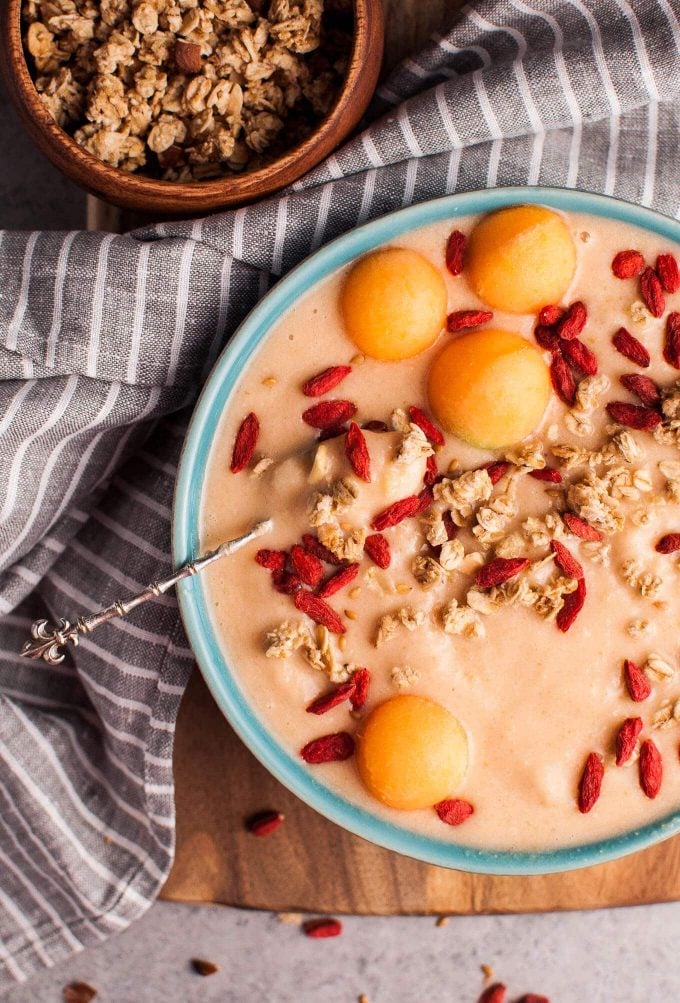 healthy cantaloupe and banana breakfast smoothie bowl with a spoon next to a grey cloth napkin