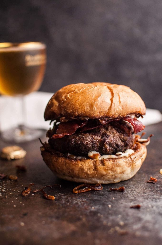 beef burger on a bun with bacon, horseradish, mayo, and fried onions