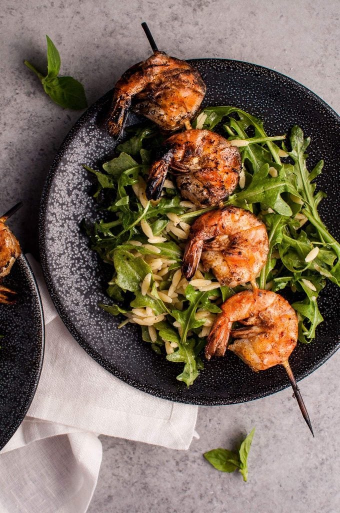 plate with smoky grilled shrimp on a skewer on a bed of arugula and orzo