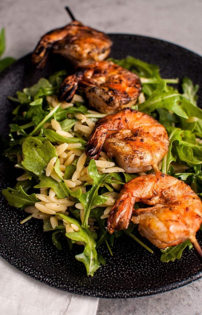 close-up of smoky grilled shrimp, orzo, and arugula with garlic lemon dressing on a plate