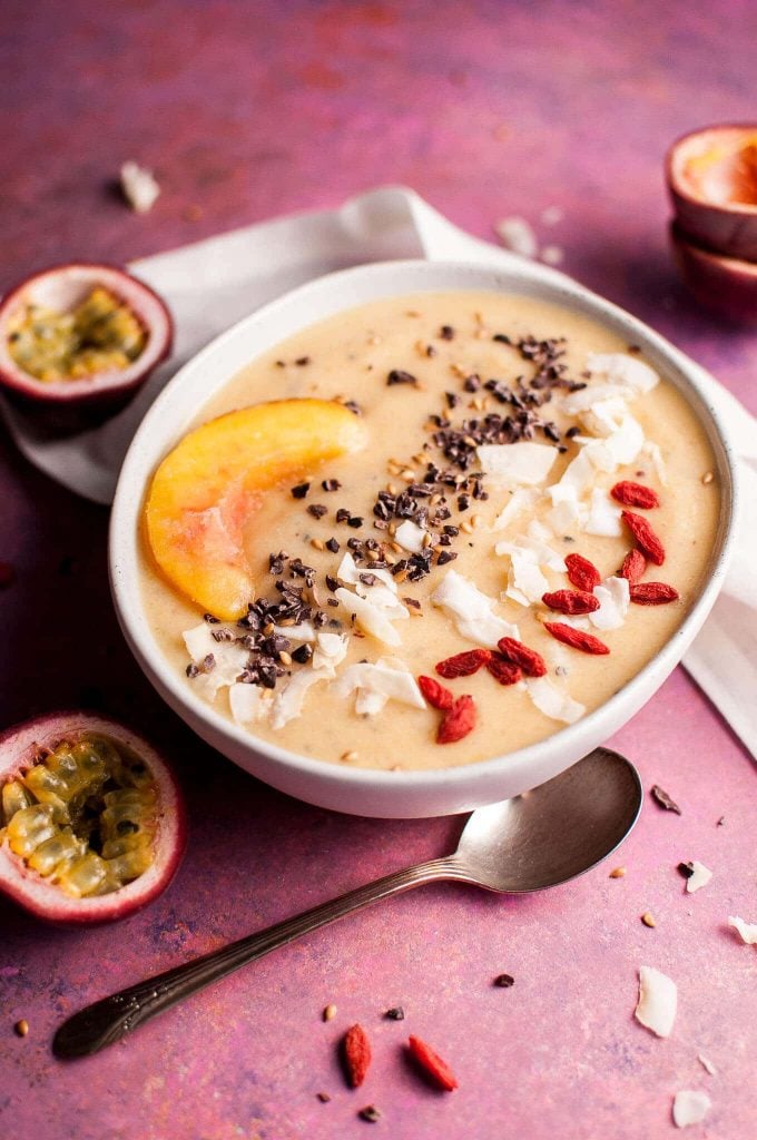 white bowl of peach and passion fruit smoothie bowl recipe next to a spoon