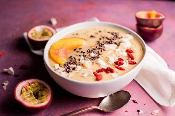 peach and passion fruit smoothie bowl topped with peach slice next to spoon