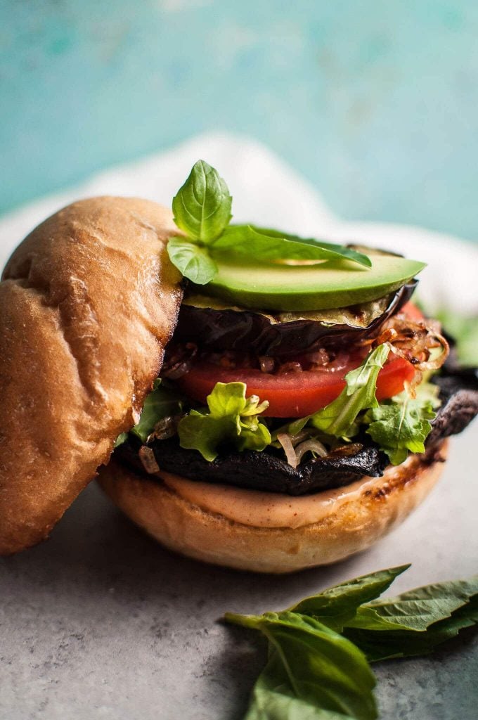 close-up of grilled mushroom and eggplant burger with avocado and top of bun resting beside it