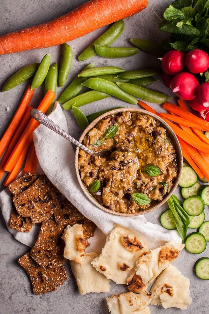 roasted eggplant dip in a bowl with a spoon next to raw vegetables and crackers