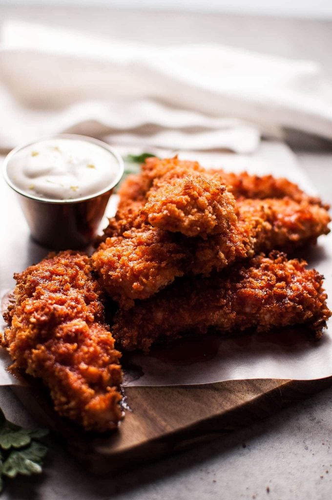 pile of sriracha honey chicken tenders on a board with a small container of mayo lime dipping sauce