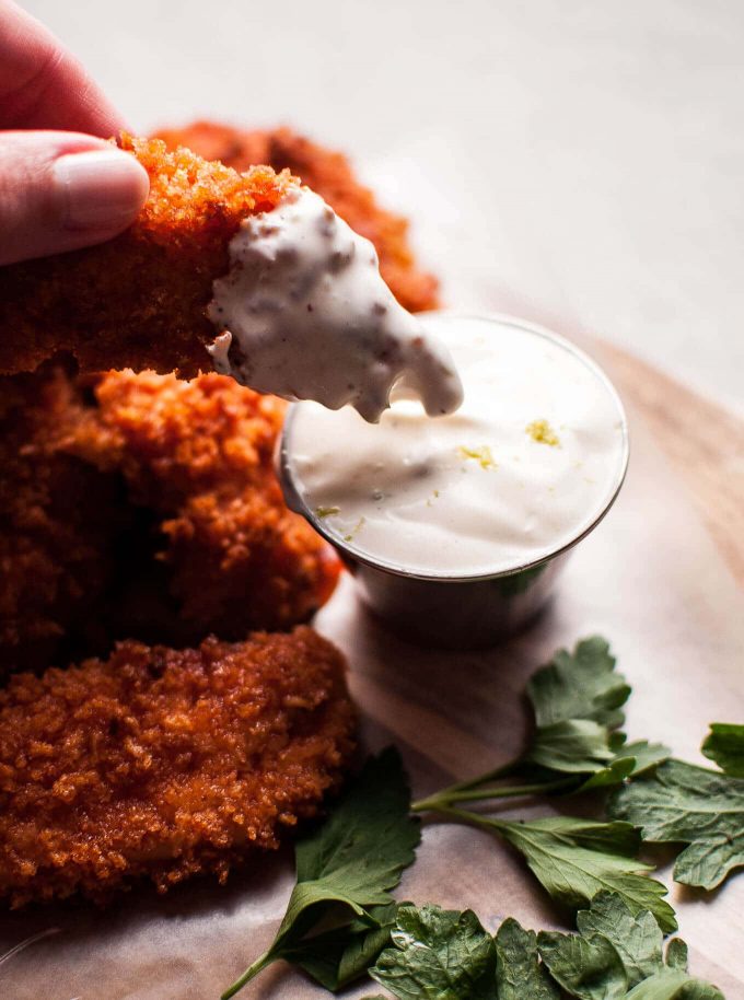 a hand dipping a spicy sriracha honey chicken tender into lime mayo sauce