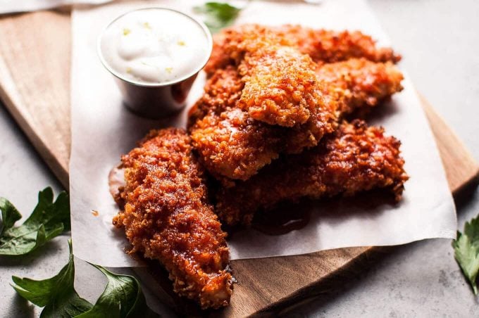 pile of spicy and sweet sriracha honey oven-baked chicken tenders beside a container of refreshing lime mayo dip