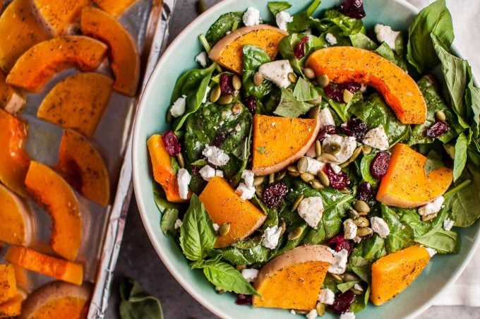 bowl of butternut squash and spinach salad beside pan of roasted squash