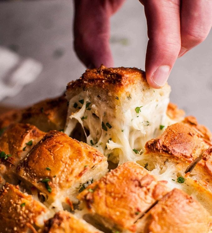a hand pulling out a piece of parmesan cheese and garlic pull-apart bread