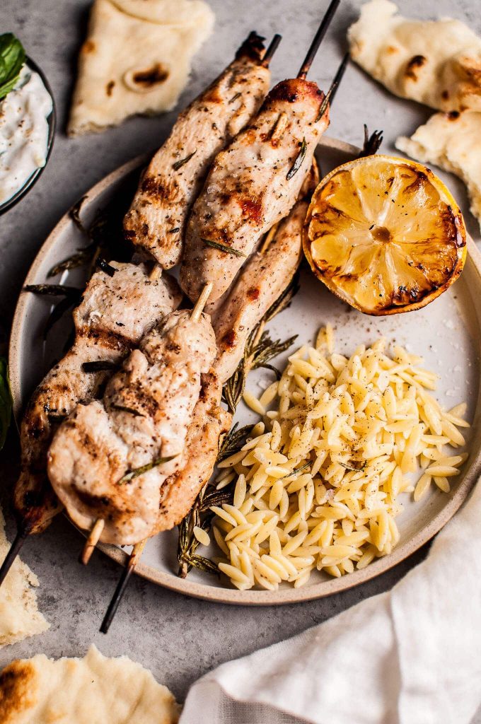 plate with rosemary chicken skewers, charred lemon slice, and orzo