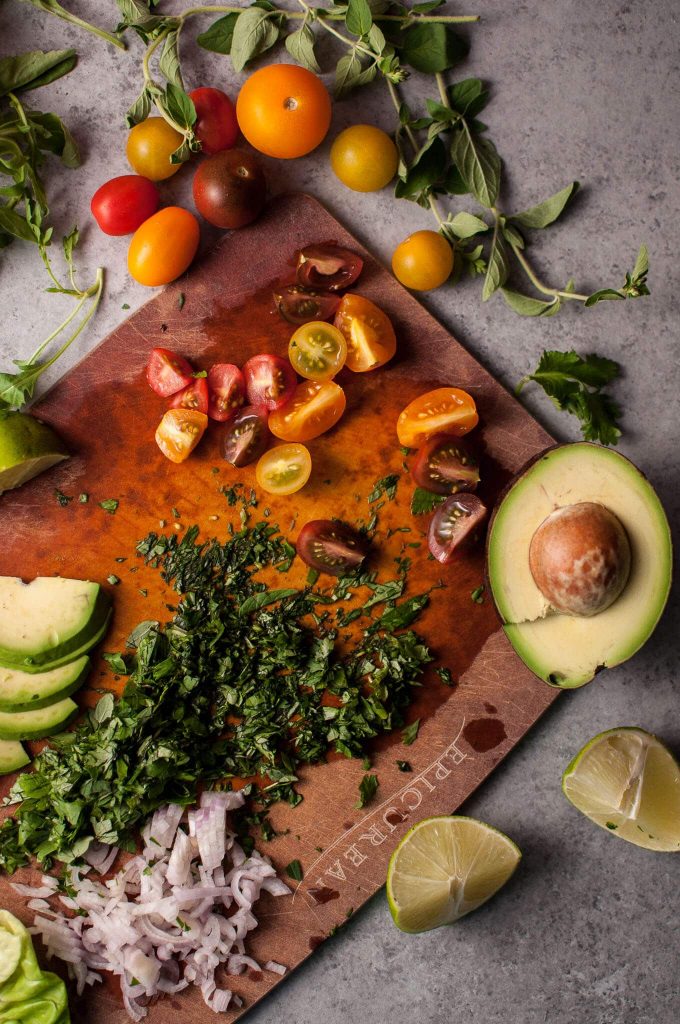 cutting board with avocado, tomatoes, and herbs