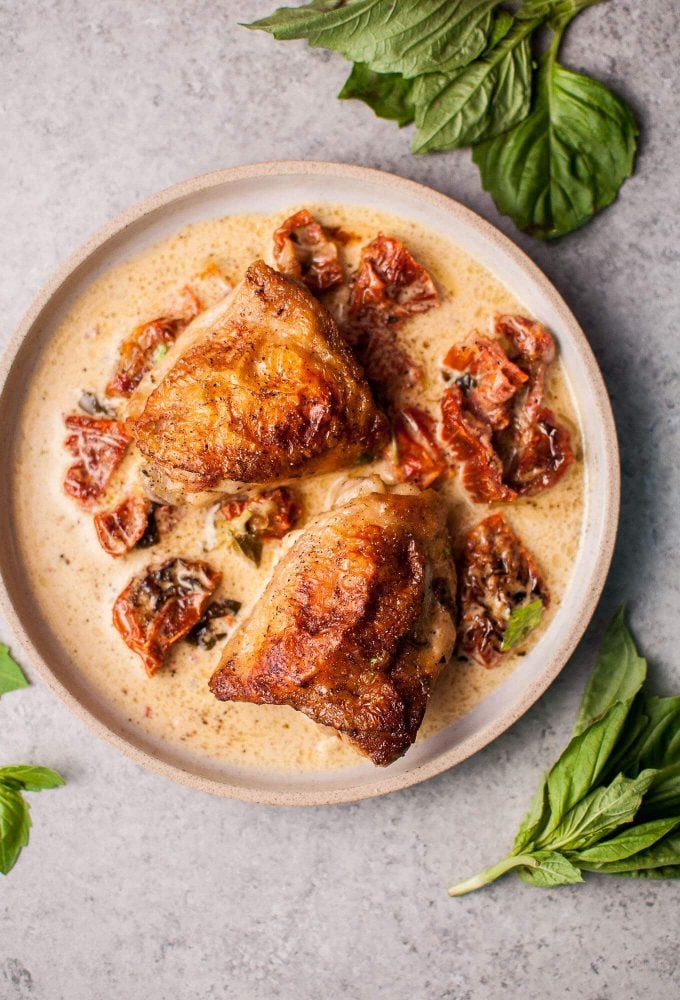 plate with two creamy chicken thighs with sun-dried tomatoes and basil