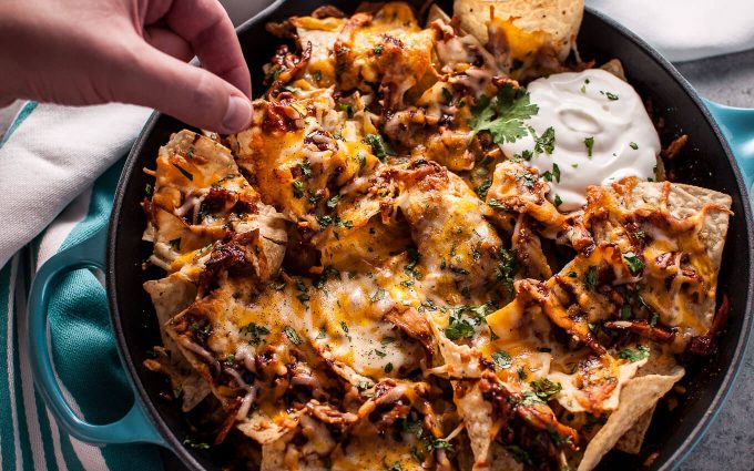 hand reaching into skillet with BBQ chicken nachos with cheese